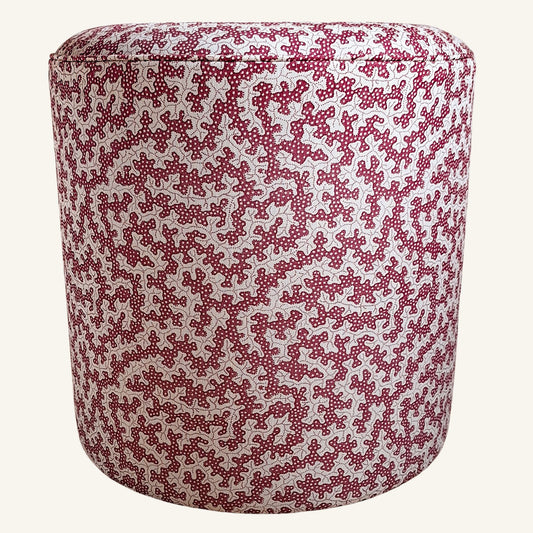 A cylindrical upholstered ottoman or stool with a dense red and white abstract floral pattern, shown against a plain off-white background.