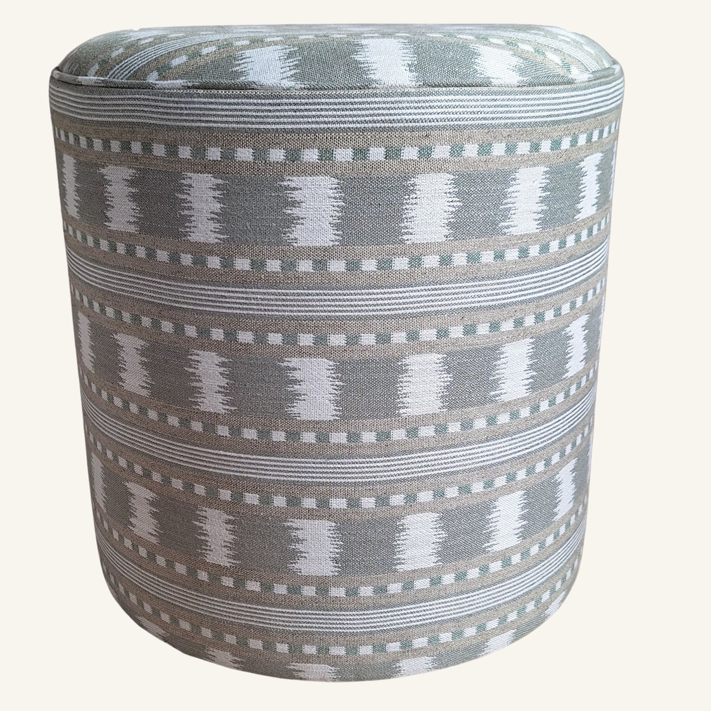 A cylindrical upholstered ottoman or pouffe with a grey, white, and green geometric ikat-style woven pattern, shown against a solid off-white background.