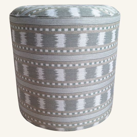 A cylindrical upholstered ottoman or pouffe with a grey, white, and green geometric ikat-style woven pattern, shown against a solid off-white background.