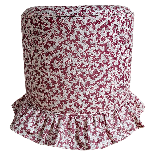 A cylindrical upholstered stool or ottoman with a pink and white floral pattern and a ruffled skirt base, shown against a plain white background.