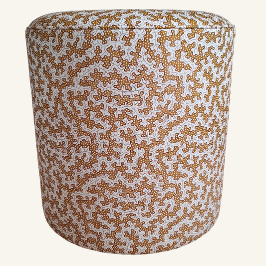 A cylindrical upholstered pouf or ottoman with a dense abstract pattern in warm brown and orange on a white background, shown against a solid off-white backdrop.